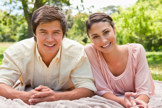 Man and a woman smiling while lying on their front on top of a grey blanket 