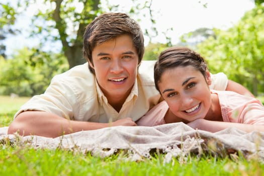 Man and a woman smiling as they lie on their front on top of a grey blanket together