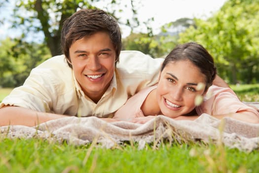 Man and a woman smiling and looking straight in front of them while lying prone on a grey blanket