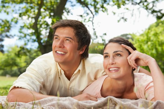 Man and a woman looking towards the sky while lying prone on a grey blanket in the grass