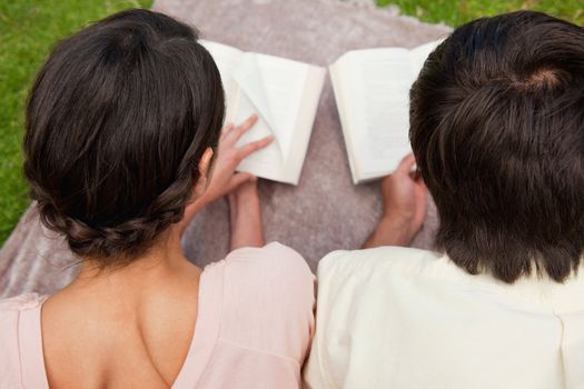 Rear view of a man and a woman reading books while lying prone on a blanket in the grass