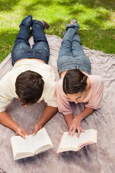 Elevated view of a man and a woman reading books while on a lying next to each other on a blanket in the grass