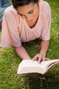 Woman looking down while reading a book as she is lying down in grass