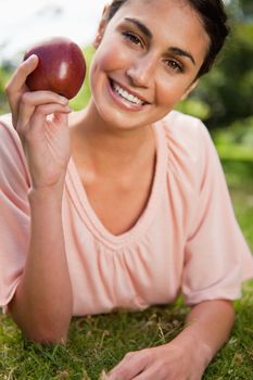 Woman smiles while holding a red apple as she is lying prone in grass