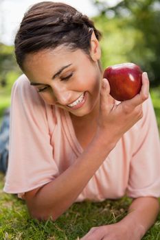 Woman looking down towards the ground while presenting a red apple as she is lying down in grass