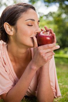Woman with her eyes closed smells a red apple while lying prone in grass