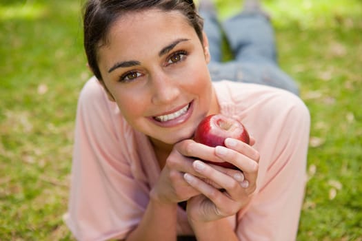 Woman looking in front of her while holding a red apple as she lies prone in grass