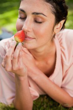 Young woman with he eyes closed smelling an strawberry while lying prone in grass