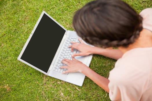 Woman uses a laptop while lying on her front in grass