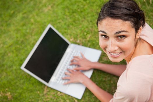 Woman looks towards her side while using a laptop as she lies prone in grass