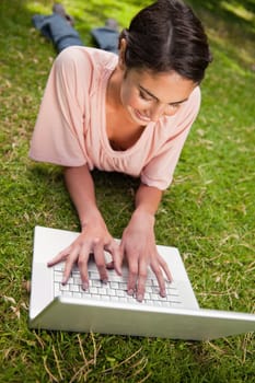 Smiling woman using a white laptop as she is lying prone in grass