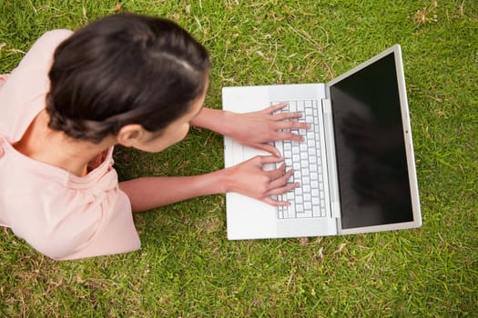 Elevated view of a woman while she uses a white laptop as she is lying prone in grass
