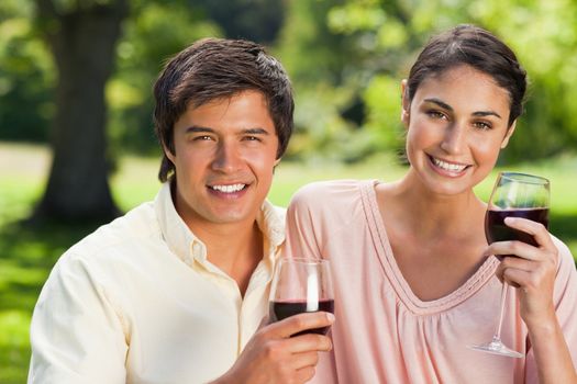 Woman and a man looking straight ahead while holding glasses of red wine in a park