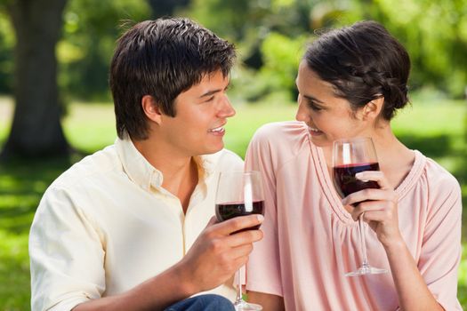 Man and a woman looking at each other while each holding glasses of red wine in a park