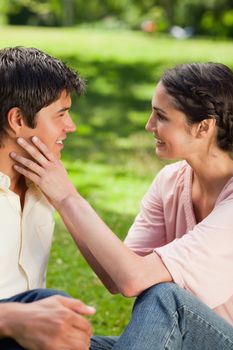 Woman smiling as she embraces her friends face with her hands in a park