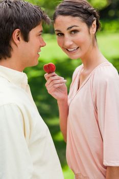 Woman looks towards the side while offering her friend a strawberry in a park
