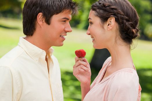 Man smiling as he is being offered a ripe strawberry by his friend in a park