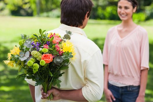 Man preparing to surprise his friend by giving her a bunch of flowers with focus on the man and the flowers