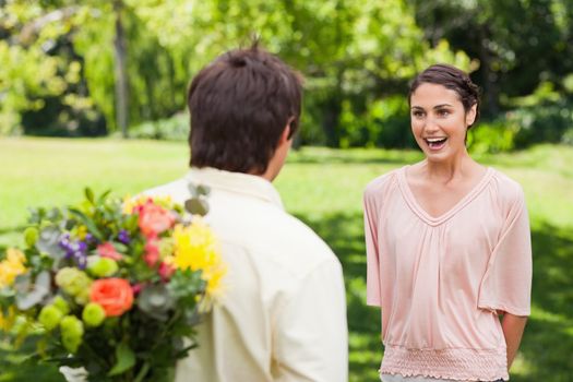 Woman excited as she approaches her friend who has flowers hidden behind his back