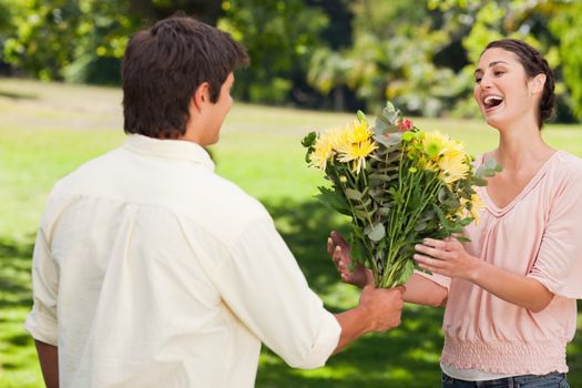 Man present his surprised friend with a bouquet of flowers in a park