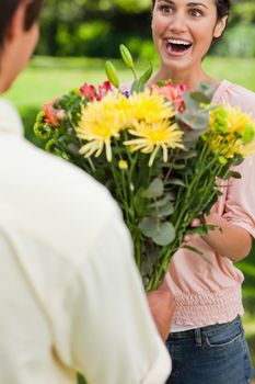 Woman with a surprised expression is presented with a bouquet of flowers by her friend 