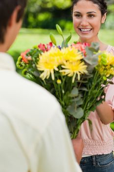 Woman smiling happily as her friend presents her with a bouquet of colourful flowers