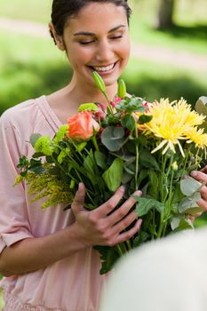 Woman smiling as she looks at a bouquet flowers which have been given to her a friend