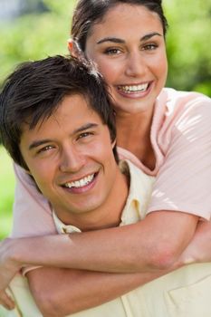 Close-up of woman smiling while looking in front of her as she is being carried bey her friend in a park