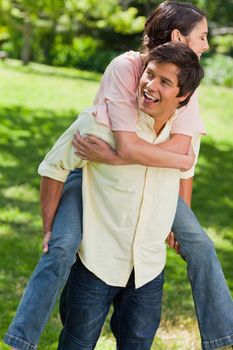 Man smiling and looking towards the side while he is carrying his friend on his back in a park