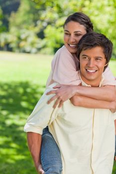 Woman smiling while holding her friends shoulders tight as he is carrying her on his back in a park