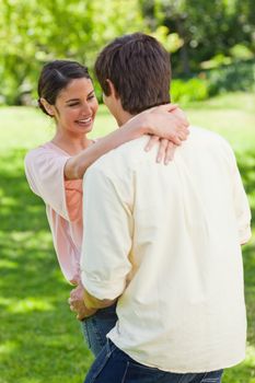 Woman laughing as she is holding onto the back of her friends neck in a park