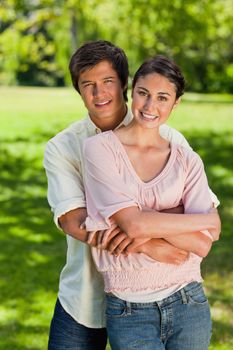 Man and woman smiling as he has his arms around her abdomen in a park