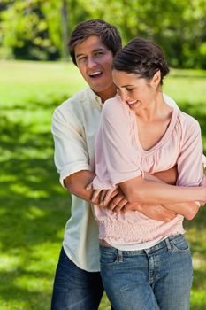 Woman laughing as her friend is holding her in a hug from behind with their arms joined at her abdomen