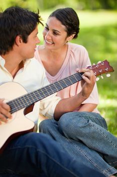 Man playing a guitar and looking at his smiling friend while sitting on grass with her