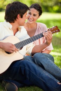 Woman smilng while looking at her friend who is playing the guitar as they both sit on the grass