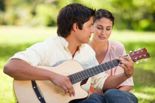 Woman listens to her friend play the guitar as they both sit next to each other on the grass