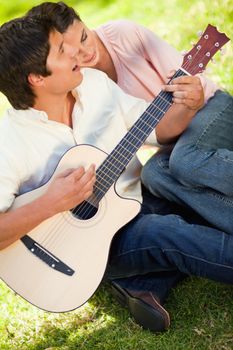 Man singing while playing the guitar as his friend leans on his shoulder while listening