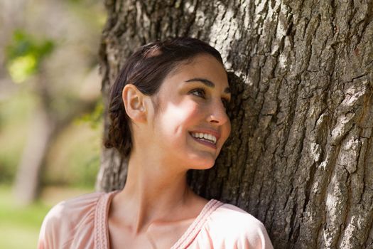Woman looking over her left shoulder and smiling while sitting against the trunk of a tree