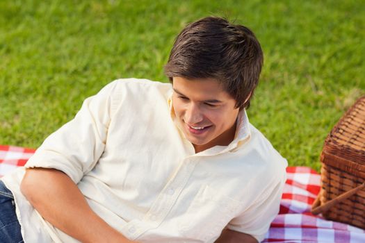 Man smiling as he lies on his side next to a basket on a red and white picnic blanket in the grass