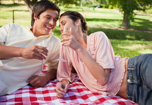 Man and a woman laughing happily and raising their glasses in toast while lying on a red and white picnic blanket