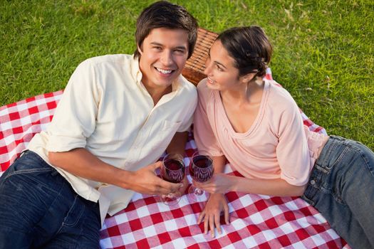 Woman smiling as she looks at her friend while holding glasses of red wine during a picnic