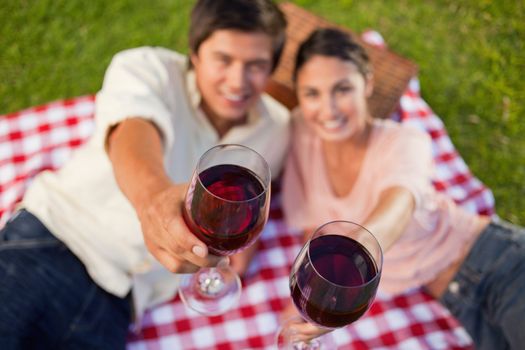 Man and a woman raising their glasses of red wine during a picnic with focus on the glasses of wine