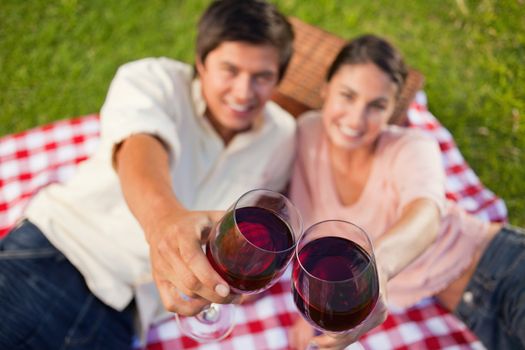 Man and a woman touching their glasses of red while raised during a picnic with focus on the glasses of wine
