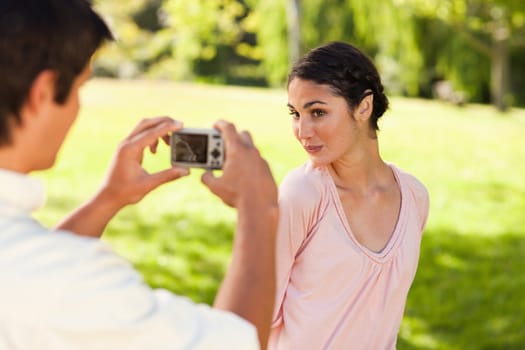 Using a camera, the man takes a photo of his friend smiling while she poses for the photo in a park