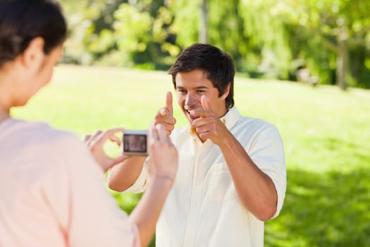 Using a camera, the woman takes a photo of her friend smiling while her poses for the photo in a park
