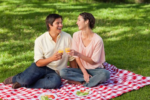 Man and a woman laughing while raising their glasses of orange juice during a picnic
