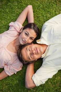 Woman with their eyes open lying head to shoulder with her arm resting behind her neck on the grass