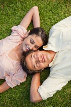 Woman looking at her friend while lying head to shoulder with her arm resting behind her neck on the grass