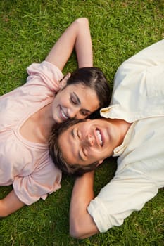 Woman looking at her smiling friend while lying head to shoulder with her arm resting behind her neck on the grass