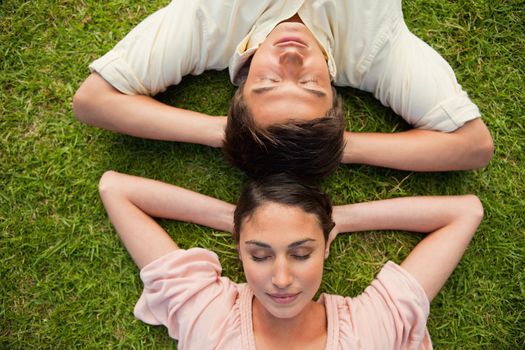 Close-up of a man and a woman with their eyes closed lying head to head with both of their arms resting behind their neck on the grass